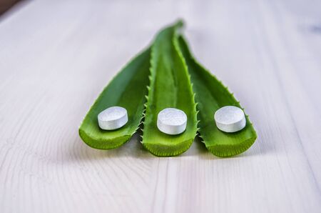 Close-up of slices of fresh aloe vera on white background and pillsの写真素材