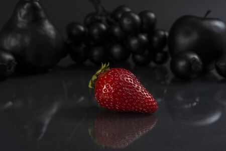 Conceptual image of black fruits on gray reflective surface with a red strawberry in frontの写真素材