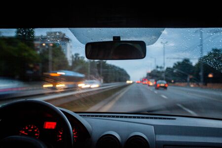Road view from inside car natural light street and other cars is motion blurred during rain at duskの写真素材