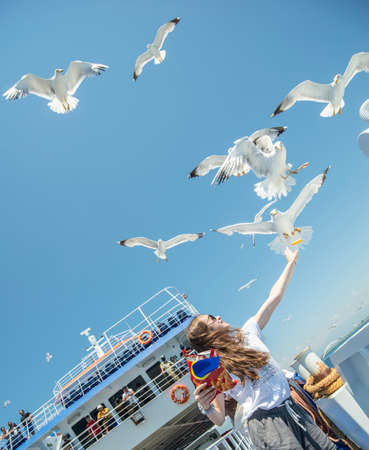 Two young girls feeding seagulls on sunny day on a shipの写真素材