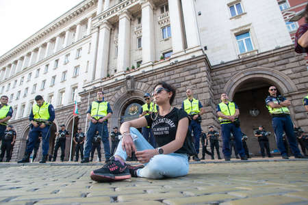 Sofia, Bulgaria - Jul 21 2020: A protester sitting on the pavement in front of police officers on Nezavisimost square during the anti-government protestsのeditorial素材