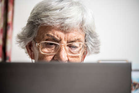 An elder lady with glasses staring at laptop's monitor while clicking with a mouseの写真素材