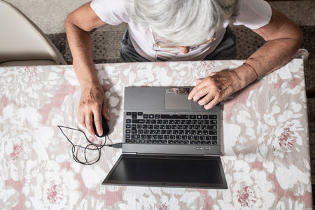An elder lady with glasses staring at laptop's monitor while clicking with a mouse