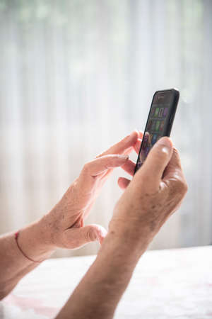 An elder lady touching something on the screen while holding a smartphone with one handの写真素材