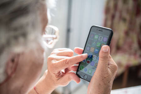 An elder lady touching something on the screen while holding a smartphone with one handの写真素材