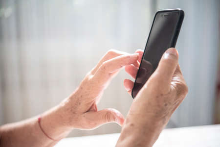 An elder lady touching something on the screen while holding a smartphone with one handの写真素材