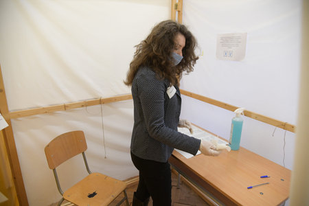 Sofia, Bulgaria - Apr 4 2021: A woman in protective mask and gloves is cleaning the voting desk with...