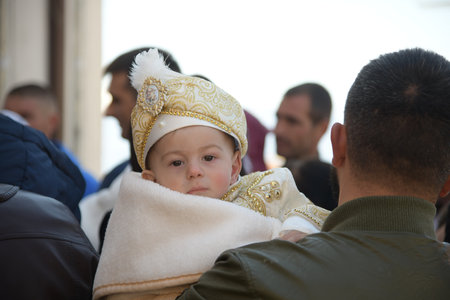 Ribnovo, Bulgaria - Apr 11 2021: A small boy dressed festively is looking sad while his father is carrying him to be circumventedのeditorial素材