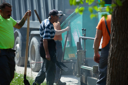 Mihaltsi, Bulgaria - May 7 2021: A worker with a shovel going to get for some asphalt from the paver