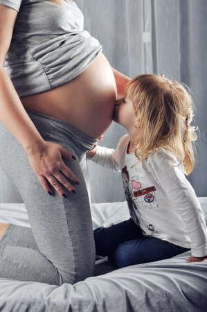 Little girl kissing her mothers pregnant bellyの写真素材