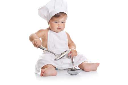 Funny adorable baby boy chef sitting and playing with kitchen equipment on a white backgroundの写真素材