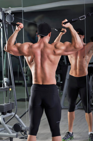 Handsome powerful athletic man doing biceps exercise with cables. Strong bodybuilder with perfect...