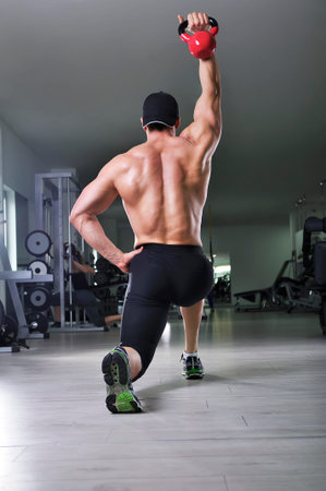 Handsome powerful athletic man doing complex exercise with kettle bell. Strong bodybuilder with ...