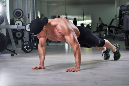 Handsome powerful athletic man performing push ups at the gym. Strong bodybuilder with  perfect...
