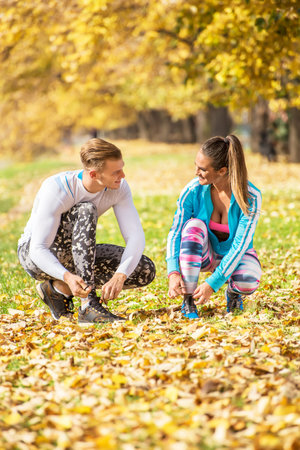 Beautiful young couple preparing their shoes for run in the park. Autumn environment.の写真素材