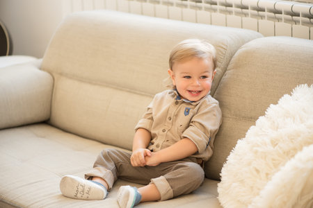 Nicely dressed and happy little boy with blue eyes sitting on the sofa.の写真素材