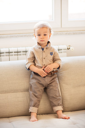 Nicely dressed little boy with blue eyes standing up on the sofa.の写真素材
