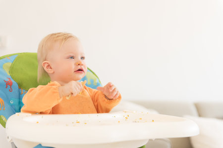 Portrait of adorable baby girl with blue eyes sitting in the highchair and have a lunch.