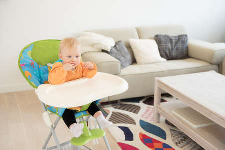 Adorable baby girl with blue eyes sitting in the highchair. Ready for eating.の写真素材