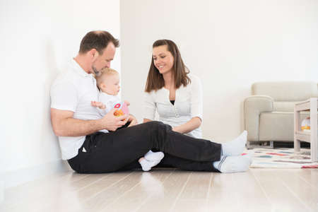 Happy family of three  is enjoying at home. Parents and their beautiful baby girl sitting on the ground and playing. Family values. Leisure together.の写真素材