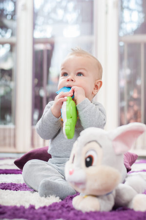 Happy baby boy sitting on the floor and playing with his toy.