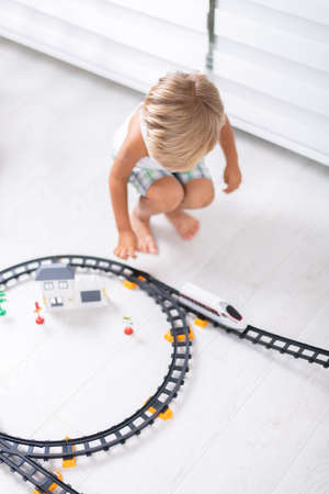 Cute kid boy playing with toy railway road at home on the floorの写真素材