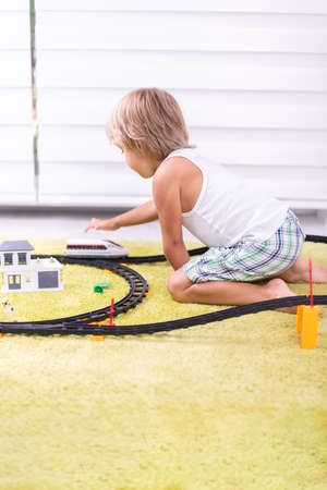 Cute kid boy playing with toy railway road at home on the floorの写真素材