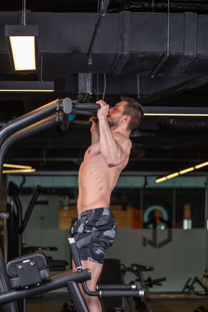 Muscular sexy young man doing exercise for the back on horizontal bar. Side viewの写真素材