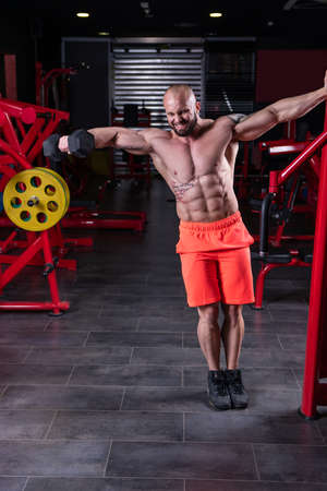 Powerful muscular man doing exercise for shoulder with dumbbell at the gymの写真素材