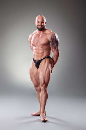 Sexy muscular bodybuider posing on the gray backgroundの写真素材