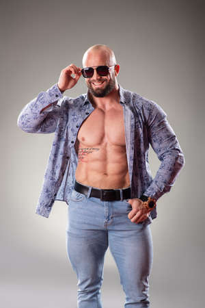 Sexy unbuttoned muscular bodybuider with sunglasses on the gray backgroundの写真素材