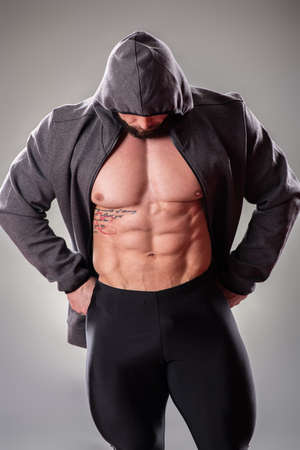 Sexy muscular bodybuider posing with sweatshirt and hood on the gray backgroundの写真素材