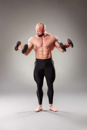 Sexy muscular bodybuider posing with weights on the gray backgroundの写真素材