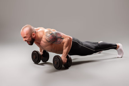 Sexy muscular bodybuider doing push ups with weights on the gray background