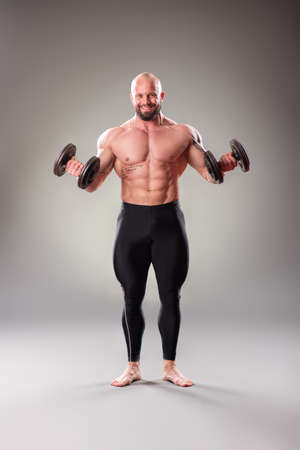 Sexy muscular bodybuider posing with weights on the gray backgroundの写真素材