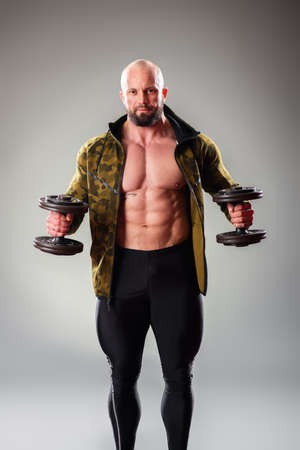 Sexy muscular bodybuider posing with sweatshirt and lifting weights on the gray background.の写真素材