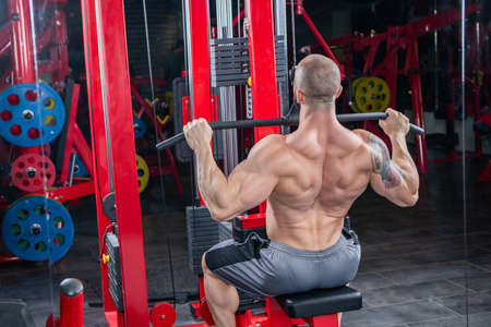 Powerful muscular man doing exercise for back on the lat machineの写真素材