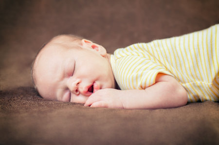 Beautiful newborn baby boy sleeping peacefully on the soft brown blanket