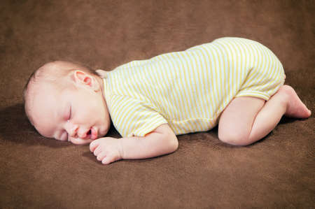 Beautiful newborn baby boy sleeping peacefully on the soft brown blanketの写真素材