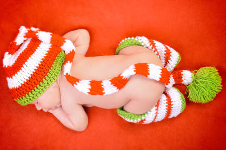 Beautiful newborn baby boy with cute cap sleeping peacefully on the soft red blanketの写真素材