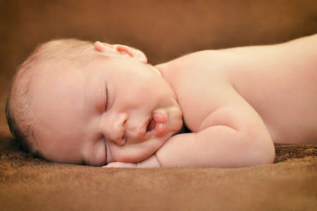 Beautiful newborn baby boy sleeping peacefully on the soft brown blanketの写真素材