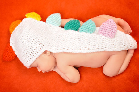 Beautiful newborn baby boy with cute cap sleeping peacefully on the soft red blanket