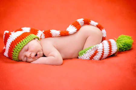 Beautiful newborn baby boy with cute cap sleeping peacefully on the soft red blanketの写真素材