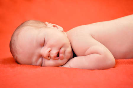 Beautiful newborn baby boy sleeping peacefully on the soft red blanketの写真素材