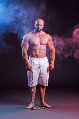 Powerful muscular man shirtless posing with chain. Studio shoot with red and blue smokeの写真素材