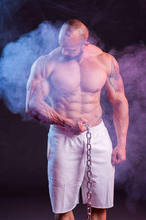 Powerful muscular man shirtless posing with chain. Studio shoot with red and blue smokeの写真素材