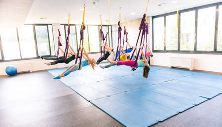Group of young women and one muscular man making antigravity yoga exercises. Fly fitness. Purple hammockの写真素材