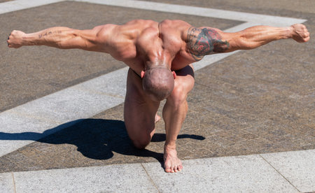 Powerful muscular bodybuilder in panties posing at the park. Kneeling with contraction of shoulders...