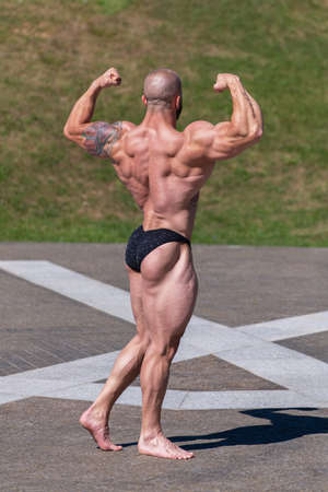Powerful muscular bodybuilder in panties posing at the park. Back and biceps contractionの写真素材