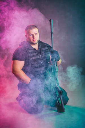 Soldier comes out of the smoke on the battlefield. The concept of military special operations. Kneeling and posing with shotgunの写真素材